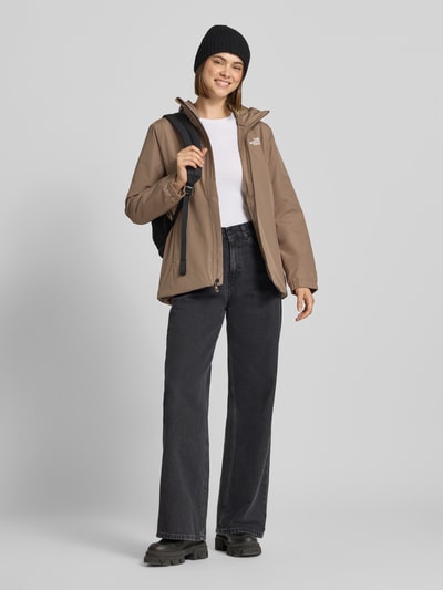 Frauenmodel trägt Regular Fit Funktionsjacke mit Logo-Print Modell 'Quest Mono' von The North Face in Beige, kombiniert mit schwarzer Hose, Ganzkörperansicht von vorne. Damen Funktionsjacke mit Kapuze, Reißverschluss, Regular Fit, Rückenlänge 69 cm, Schulterbreite 40 cm, Brustweite 40 cm, Ärmellänge 63 cm.
