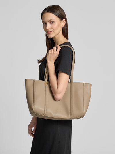 Frauenmodel trägt Shopper mit Label-Detail von CK Calvin Klein in Beige, strukturierte Oberfläche, Tragehenkel, Ganzkörperansicht von vorne. Hauptfach mit Reißverschluss, Innenfach, Maße: 48x27x16 cm, Schulterriemen 63 cm.