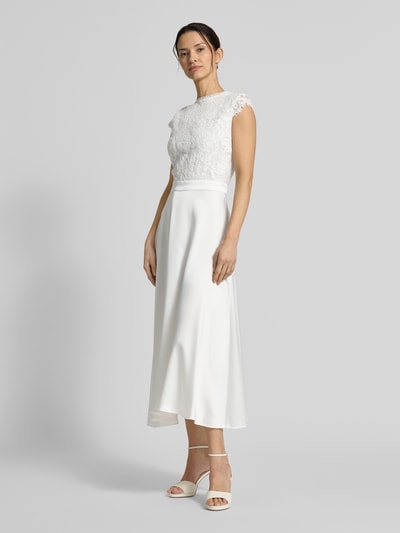Frauenmodel trägt Brautkleid in Midilänge Modell 'Lilia' von GUIDO MARIA KRETSCHMER WOMAN in Weiß, Oberteil aus Spitze, Rock aus Satin, Ganzkörperansicht von vorne.