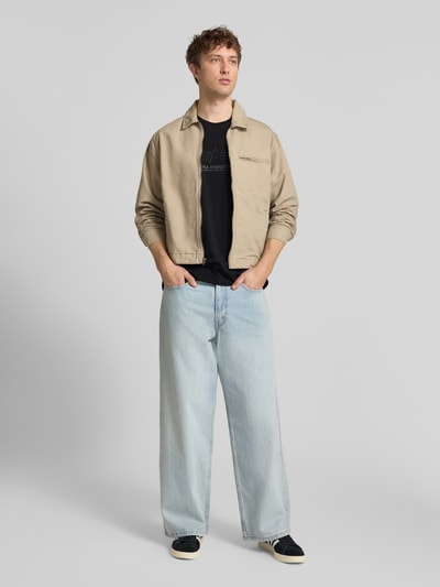 Mężczyzna nosi T-Shirt aus Baumwolle Modell 'BASIC' od Alpha Industries, czarne, bawełniane, prosty krój, okrągły dekolt, widoczne detale labela, długość tyłu w rozmiarze M 67 cm, widok całej sylwetki z przodu.