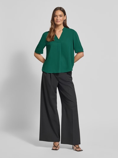 Modelka kobieca nosi Regular Fit Bluse mit V-Ausschnitt od Marc Cain, kolor zielony, stójka, krój regular fit, długość tyłu 59 cm, długość rękawa 29 cm, widok całej sylwetki od przodu.