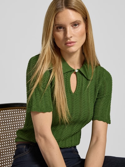 Frauenmodel trägt Strickshirt mit Umlegekragen und Schlüsselloch-Ausschnitt von Scotch & Soda, schmaler Schnitt, Baumwoll-Mix, 1/2-Arm, gerippte Textur, Farbe Grün, Nahaufnahme Oberkörper.
