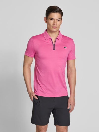 Męski model nosi Slim Fit Poloshirt aus schnelltrocknendem Material von Lacoste Sport, różowy, krótki rękaw, logo, krój slim fit, zdjęcie całej sylwetki z przodu.