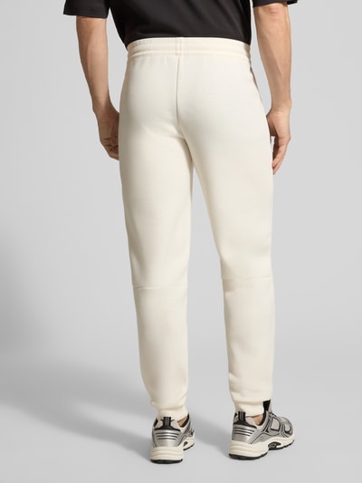 Männermodel trägt Sweatpants mit Viskose-Anteil Modell 'TRAIN PREMIUM SHIELD' von EA7 Emporio Armani in Creme, Ganzkörperansicht Rückansicht.