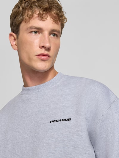 Männermodel trägt Relaxed Fit Sweatshirt aus Baumwoll-Mix von PEGADOR in Hellgrau mit Logo-Stickerei, Nahaufnahme Oberkörper.