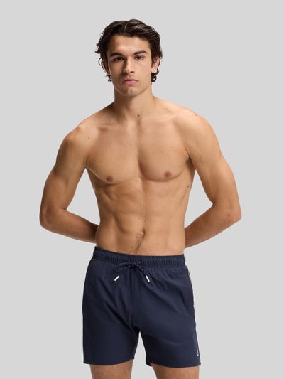 Mannenmodel draagt Badeshorts met tunnelkoord model 'ICONIC' van BOSS, effen, labelprint, contrasterende strepen, elastische tailleband, zijzakken, achterzak, blauwe kleur, gladde textuur, vooraanzicht van het hele lichaam