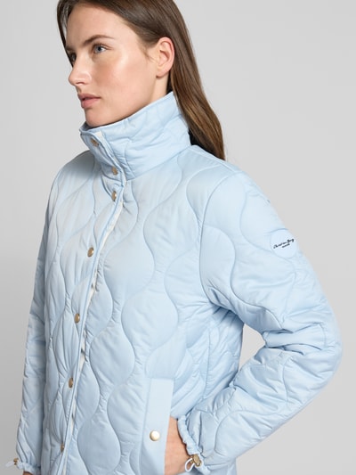 Frauenmodel trägt Regular Fit Steppjacke mit gefüttertem Stehkragen von Christian Berg Woman Selection in Hellblau, Nahaufnahme Oberkörper. Stepp-Optik, durchgehende Knopfleiste, Eingrifftaschen, dezentes Marken-Detail am Ärmel, glatte strukturierte Oberfläche.