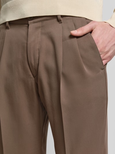 Männermodel trägt Straight Fit Stoffhose aus Lyocell-Mix Modell 'Leek' von Drykorn in Braun mit Bügelfalten, Nahaufnahme Hüftbereich.