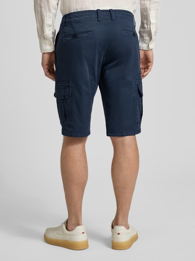 Männermodel trägt Bermudas mit Cargotaschen von bugatti in Dunkelblau, Regular-Fit, Knopf- und Reißverschluss, Ganzkörperansicht Rückansicht. Kontext: Herren Bermudas, Gesäßtaschen, Bundweite 45 cm, Innenbeinlänge 30 cm bei Größe 50.