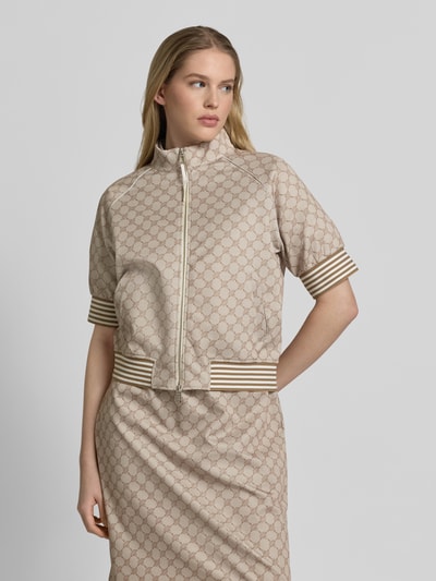 Frauenmodel trägt Jacke mit 1/2-Arm Modell 'Tayla' von JOOP!, beigefarbener Material-Mix, Logo-Muster, Stehkragen, Nahaufnahme Oberkörper.