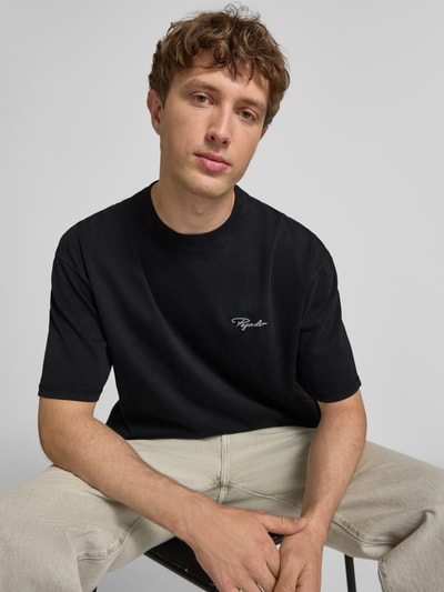Męski model nosi Oversized T-Shirt mit Label-Stitching od Pegador, czarny kolor, czysta bawełna, okrągły dekolt, oversize, zdjęcie z przodu, zbliżenie na górną część ciała. Długość pleców w rozmiarze M: 70 cm.
