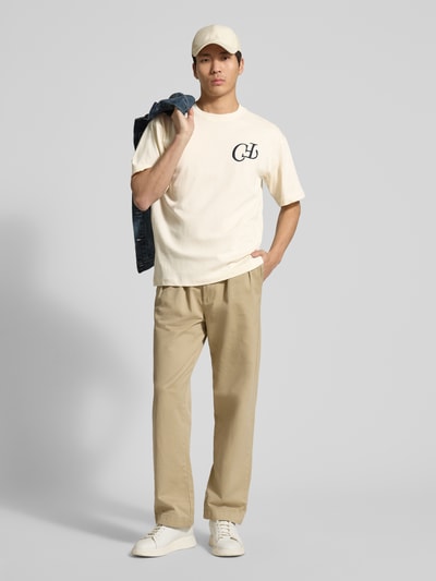 Männermodel trägt t-shirt van puur katoen model 'KARLBERG' van Casual Friday in beige met labelstitching en labelprint, los model, ronde hals, ruglengte maat M 67 cm, volledige lichaamsaanzicht van voren
