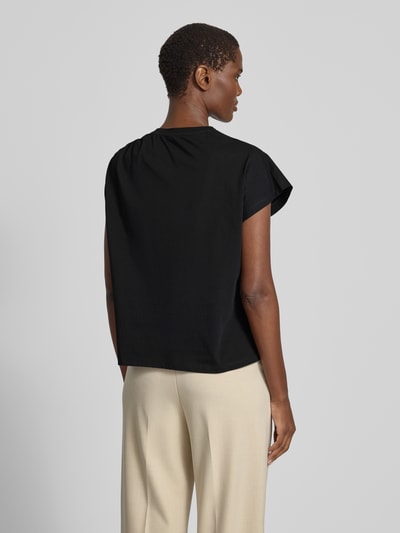 Frauenmodel trägt T-Shirt im One-Shoulder-Look Modell 'ALLIA' von Bash aus reiner Baumwolle, Regular-Fit, schwarze Farbe, Rückenlänge bei Größe S 58 cm, Ganzkörperansicht Rückansicht.