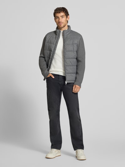 Männermodel trägt Steppjacke mit Stehkragen und Zweiwege-Reißverschluss von Christian Berg Men, graue Farbe, glatte Struktur, Ganzkörperansicht von vorne. Regular Fit, Reißverschlusstaschen, Abmessungen bei Größe M: Rückenlänge 70 cm, Schulterbreite 51 cm, Brustweite 60 cm, Ärmellänge 69 cm.