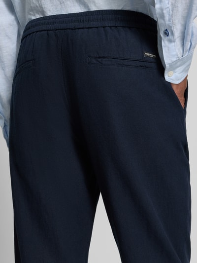 Männermodel trägt Jogpants aus Baumwoll-Leinen-Mix mit elastischem Bund von Scotch & Soda, dunkelblauer Stoff, Detailaufnahme Rückansicht, Regular-Fit, Tunnelzug, Bundweite 42 cm, Innenbeinlänge 76 cm.