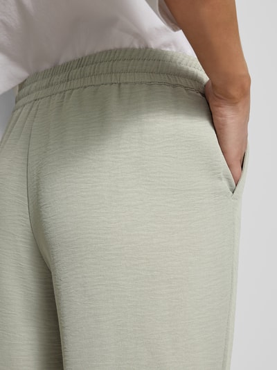 Frauenmodel trägt Jogpants mit elastischem Bund und Eingrifftaschen von Christian Berg Woman in hellgrauer Farbe, Detailaufnahme Rückenpartie. Slim Fit, elastischer Bund mit Kordelzug, französische Eingrifftaschen, Bundweite bei Größe 36: 38 cm, Innenbeinlänge bei Größe 36: 72 cm, leichte Struktur.