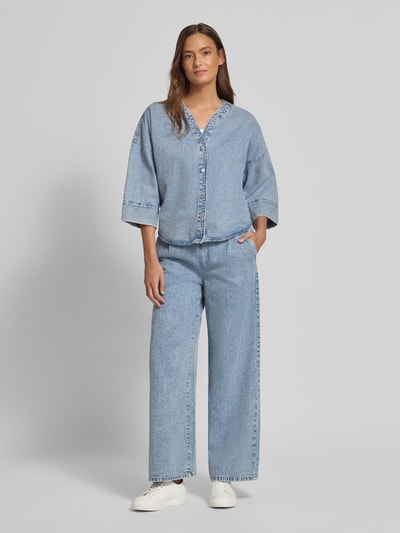 Vrouwenmodel draagt Loose Fit Jeansbluse aus Baumwoll-Viskose-Mix Modell 'VALERIA' van Vero Moda in denimlook, lichtblauw, 3/4-mouwen, knoopsluiting, mix van katoen en viscose, ganzkörperansicht van voren.