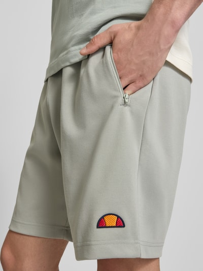 Männermodel trägt Shorts mit Label-Stitchings Modell 'BERTONI' von ellesse aus Baumwoll-Mix in hellem Grau, Nahaufnahme Oberschenkel.