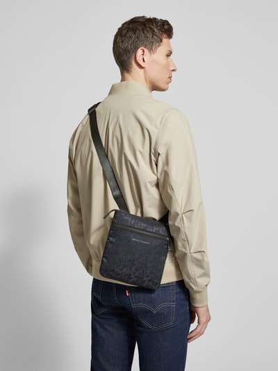 Männermodel trägt Umhängetasche mit Logo-Muster und Label-Applikation von ARMANI EXCHANGE, Beige, Blau, Ganzkörperansicht Rückansicht.