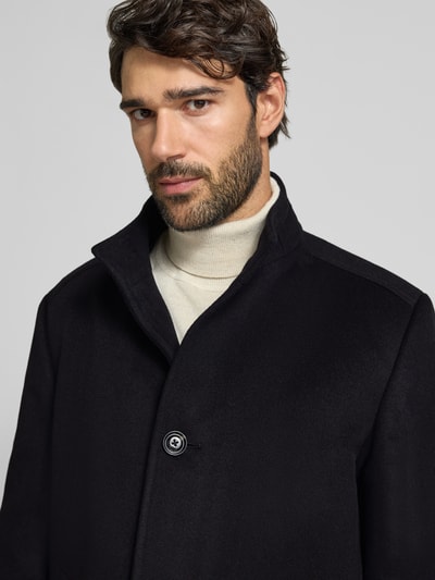 Męski model nosi Mantel mit Stehkragen Modell 'MAICO' od JOOP! COLLECTION, jednolity czarny kolor, strukturalna tkanina, stójka, zapięcie na guziki, boczne kieszenie, detale szwów i rozcięcia, materiał typu web, zbliżenie na górną część ciała.