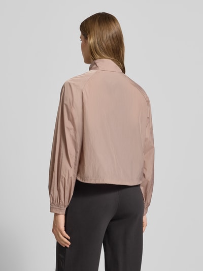 Frauenmodel trägt Relaxed Fit Jacke mit Stehkragen Modell 'Her' von PUMA in hellbraun, elastische Ärmelabschlüsse, Ganzkörperansicht Rückansicht. Kontext: Damen Jacke mit Logo-Stitching, Reißverschluss, Eingrifftaschen, Rückenlänge 55 cm, Schulterbreite 45 cm, Brustweite 56 cm, Ärmellänge 64 cm bei Größe S.