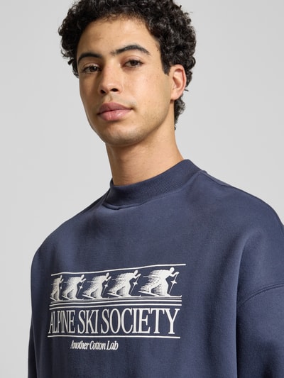 Männermodel trägt Sweatshirt mit Label-Print von Another Cotton Lab in Dunkelblau, Baumwoll-Mix, lockerer Schnitt, Nahaufnahme Oberkörper.