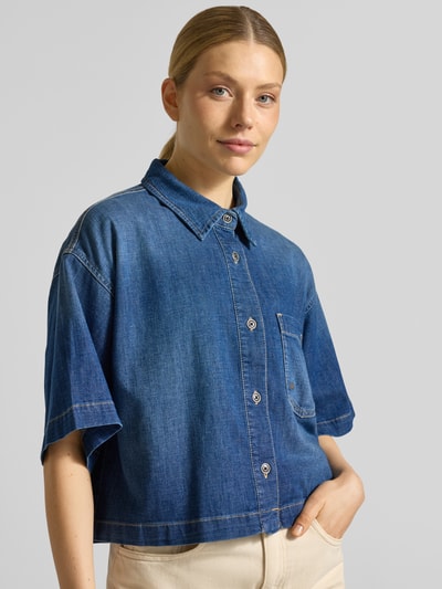 Frauenmodel trägt Boxy Fit Jeansbluse mit Brusttasche Modell 'ZURI' von Raffaello Rossi, indigoblauer Baumwoll-Mix mit Leinen-Anteil, Hemdblusenkragen, sichtbare Knopfleiste, strukturierte Oberfläche, Nahaufnahme Oberkörper.