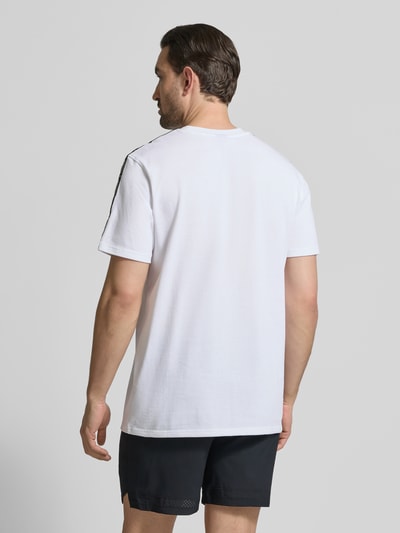 Męski model nosi Regular Fit T-Shirt mit Logo-Stitching Modell 'Icon' von Under Armour, bawełniany miks, biała koszulka, czarne spodenki, krój regular fit, widok całej sylwetki z tyłu.