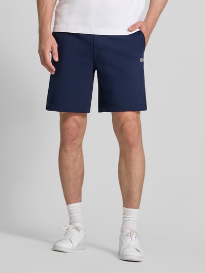 Mannenmodel draagt Regular Fit Sweatshorts uit katoenmix van Lacoste in donkerblauw met effen structuur, heren sweatshorts, detailopname vooraan.