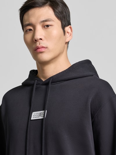 Männermodel trägt Hoodie mit Label-Stitching von MM6 Maison Margiela in Schwarz, reine Baumwolle, lockere Passform, Nahaufnahme Oberkörper.
