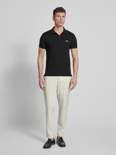 Mężczyznę model nosi Slim Fit Poloshirt aus reiner Baumwolle von Lacoste, efekt: jednolity kolor, krój slim fit, wyhaftowane logo, kołnierzyk polo, krótki rękaw, zakończenie rękawów: prążkowane, wykończenie: z bocznymi rozcięciami, wykończenie materiału: pika, materiał: bawełna, ganzkörperansicht von vorne.