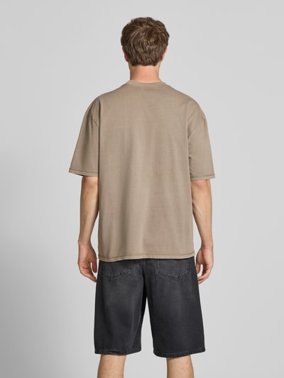 Mężczyzna model nosi Oversized T-Shirt mit Label-Stitching od Pegador, czysta bawełna, oversize, okrągły dekolt, długość pleców w rozmiarze M: 70 cm, beżowa góra, ciemne szorty, widok całej sylwetki od tyłu.