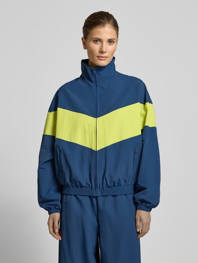 Vrouwenmodel draagt Nylon-Jacke im 90s-Stil - curated by Tinvcb van Tinvcb, blauw met gele streep, regular fit, steekzakken met rits, elastische boorden, staande kraag, rits, ruglengte 60 cm, schouderbreedte 54 cm, borstwijdte 58 cm, mouwlengte 34 cm, vooraanzicht bovenlichaam