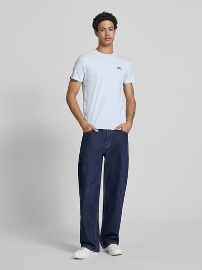 Männermodel trägt Regular Fit T-Shirt mit Logo-Stitching von Superdry, hellblau, reine Baumwolle, Rundhalsausschnitt, Ganzkörperansicht von vorne.