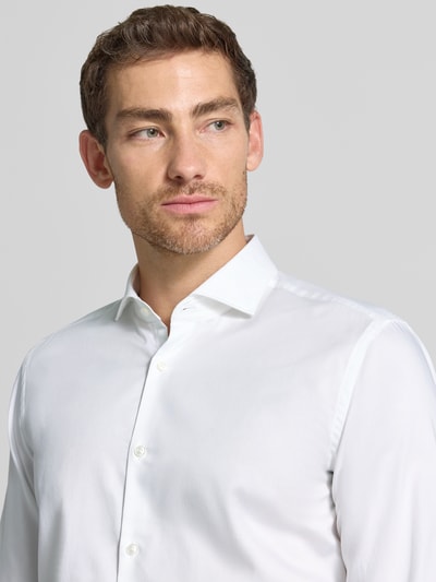 Männermodel trägt Slim Fit Businesshemd aus reiner Baumwolle Modell 'Kason' von HUGO in Weiß, glatte Textur, Nahaufnahme Oberkörper.