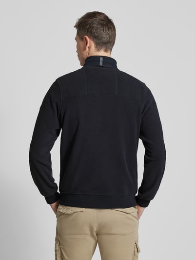 Męski model nosi Bluza rozpinana mit stójka i brustasza von camel active, krój regular fit, w kolorze czarnym, długość tyłu 68 cm, długość rękawów 67 cm, wpuszczane kieszenie zapinane na zamek błyskawiczny, widok całej sylwetki z tyłu.