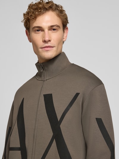 Männermodel trägt Sweatjacke aus Baumwoll-Mix von Armani Exchange in Taupe mit schwarzem Label-Print, lockerer Passform, Nahaufnahme Oberkörper.