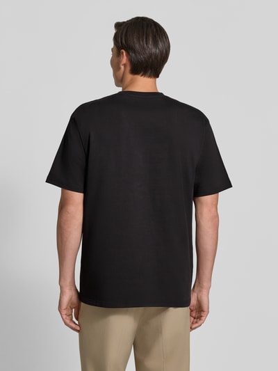 Männermodel trägt Regular Fit T-Shirt aus reiner Baumwolle Modell 'Oliver' von Wood Wood, Schwarz, glatte Textur, Ganzkörperansicht Rückansicht. Damen T-Shirt von Wood Wood, Logo-Stitching, Rückenlänge bei Größe M: 73 cm.