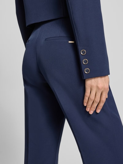 Frauenmodel trägt Hose mit Gürtel Modell 'LEILA' von Guess, Material-Mix mit Stretch-Anteil, Flared-Cut, Detailaufnahme Rückansicht.