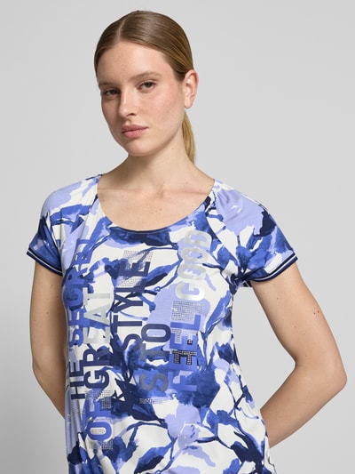 Frauenmodel trägt Damen T-Shirt aus Viskose-Mix mit Kordelzug am Saum von Betty Barclay, Blau-Weiß mit Statement-Print, Strasssteinbesatz, Regular-Fit, Rundhalsausschnitt, Stretch-Anteil, Ganzkörperansicht von vorne.