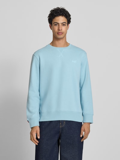Männermodel trägt Sweatshirt mit Rundhalsausschnitt und Label-Stitching von Superdry in Hellblau, Baumwoll-Mix, Regular-Fit, Ganzkörperansicht von vorne.