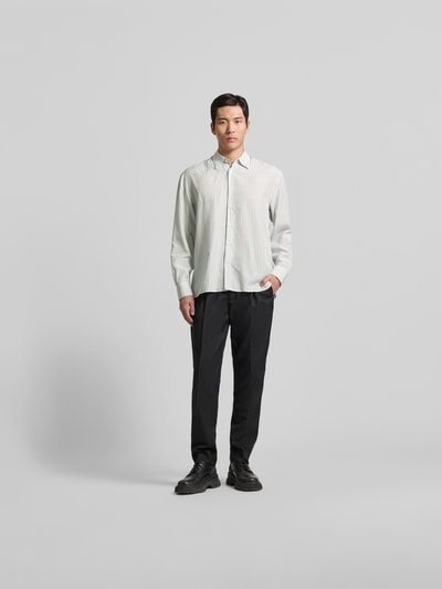 Männermodel trägt Freizeithemd aus Lyocell-Mix von Officine Générale, hell mit feinen Streifen, Regular Fit, Ganzkörperansicht von vorne.