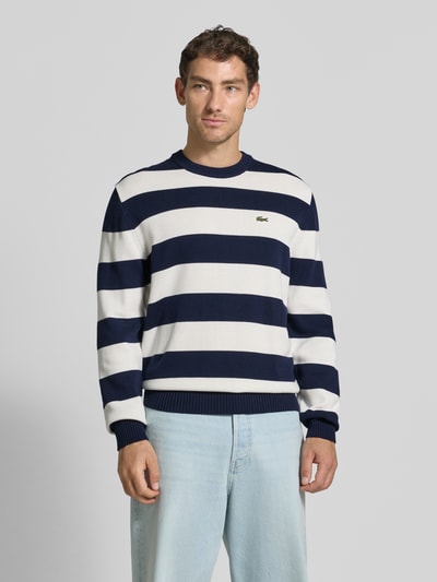 Mężczyzna nosi Regular Fit Pullover aus reiner Baumwolle od Lacoste w niebiesko-białe pasy, jasnoniebieskie spodnie, sweter z bawełny, widok z przodu, kontekst: sweter męski od Lacoste, ujęcie: całkowity widok z przodu