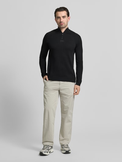 Männermodel trägt Regular Fit Troyer mit Schurwoll-Anteil Modell 'TOUR SEAMLESS QZ' von BOSS Green in Schwarz mit Reißverschluss, Ganzkörperansicht von vorne.