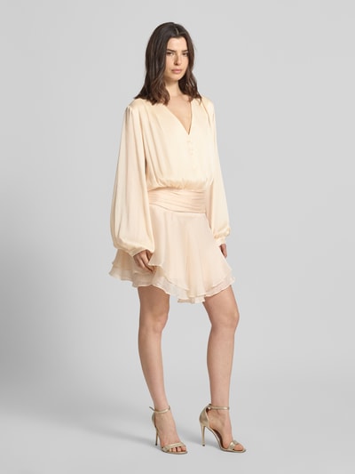 Frauenmodel trägt Minikleid mit kurzer Knopfleiste Modell 'MAGALI' von Guess, Taillierter Schnitt, V-Ausschnitt, Volantsaum in Creme, Ganzkörperansicht von vorne.
