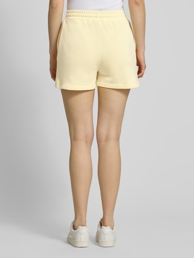 Kobiece modelka ma na sobie Regular Fit Sweatshorts aus Baumwoll-Mix Modell 'CHILLI' od Pieces, jednokolorowe jasnokremowe, z elastycznym pasem i bocznymi kieszeniami, materiał sweat, krój regular fit, widok całej sylwetki z tyłu