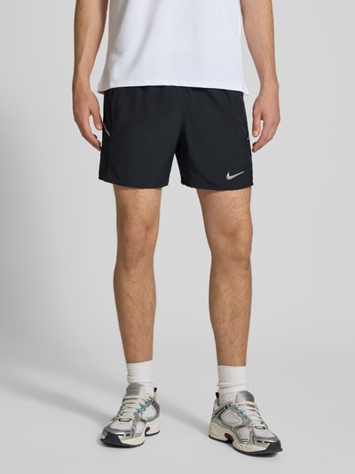 Männermodel trägt schwarze Shorts mit seitlichen Eingrifftaschen und Logo-Print von NIKE TRAINING, Loose-Fit, elastischer Bund, Nahaufnahme Oberschenkel.