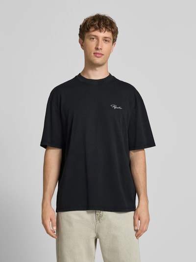 Męski model nosi Oversized T-Shirt mit Label-Stitching od Pegador, czarna bawełna, krój oversize, okrągły dekolt, długość tyłu M: 70 cm, całopostaciowy widok z przodu