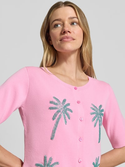 Frauenmodel trägt Strickjacke aus Viskose-Mix mit Perlen von Milano Italy in Rosa mit Palmenmotiv und Knopfleiste, Nahaufnahme Oberkörper. Damen Regular Fit, Rundhalsausschnitt, Rückenlänge 54 cm, Ärmellänge 28 cm.