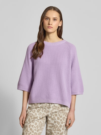 Modelka nosi Oversized Strickpullover aus reiner Baumwolle Modell 'MARGE' von JJXX w liliowym kolorze, damski sweter o splocie dzianinowym, okrągły dekolt, rękaw 3/4, wykończenia prążkowane; długość tyłu 59 cm, długość rękawa 23 cm, widok całej sylwetki z przodu.
